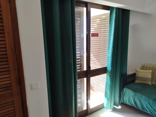 Quarto luminoso com cortinas em tons de azul-petróleo, porta de vidro para varanda e vista para o jardim na Albufeira Inn, Albufeira Portugal