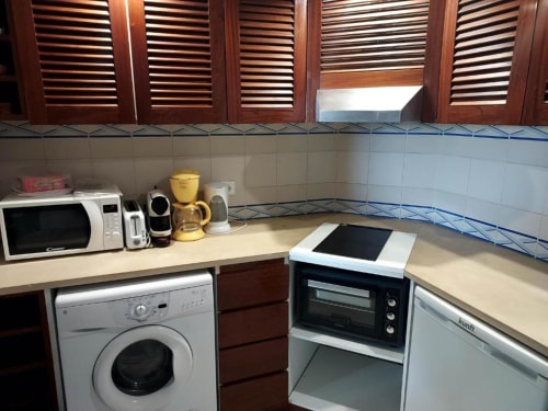 Cozinha compacta em apartamento de Albufeira com máquina de lavar, micro-ondas, forno e eletrodomésticos na bancada