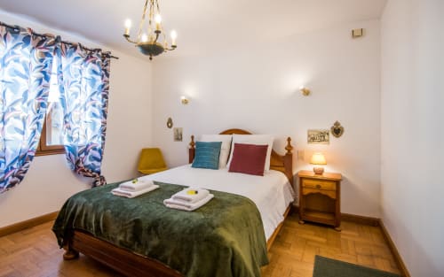Acogedora habitación en villa de Millau con cama de madera, manta verde, cortinas coloridas y accesorios de latón