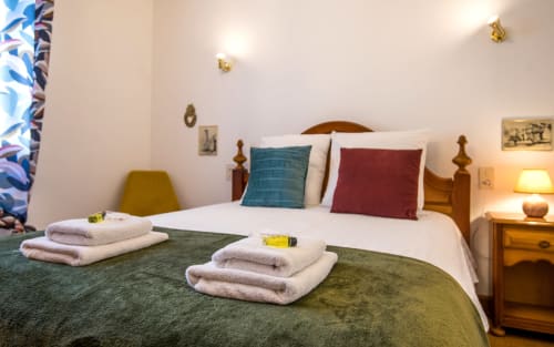 Dormitorio acogedor con sábanas blancas, almohadas coloridas y toallas enrolladas en la villa La Conciergerie en Millau, Francia