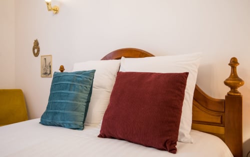 Cama con cabecero de madera y remates de latón, decorada con almohadas azules y burdeos en la villa de Millau