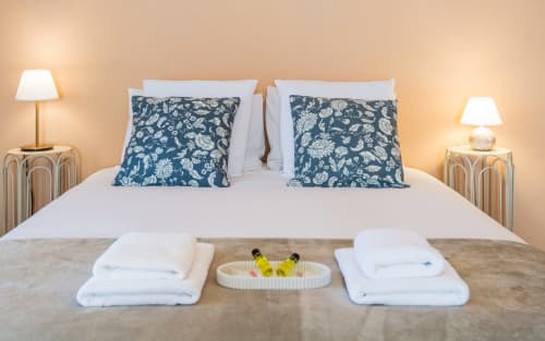Dormitorio de villa de lujo en Millau con vista a la piscina, ropa de cama blanca, almohadas con flores azules y iluminación ambiental