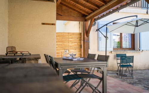 Terraza cubierta del área de comedor de la villa La Conciergerie en Millau con mesa de madera, sillas y sombrilla con vistas a la