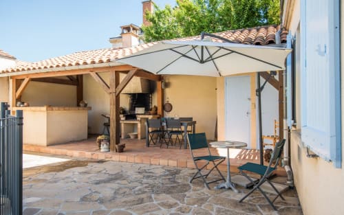 Terraza exterior de la villa La Conciergerie en Millau con zona de descanso sombreada, mesa de comedor y cocina