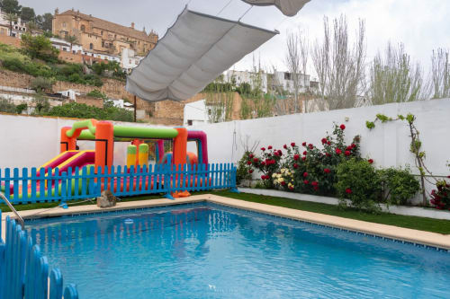 Piscina azul con castillo inflable, sombrilla y flores rojas en el hotel Las Mellis de Antequera