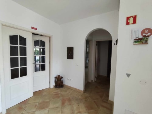 Corredor de entrada da Albufeira Inn com portas brancas, arco decorativo e piso de azulejo terracota