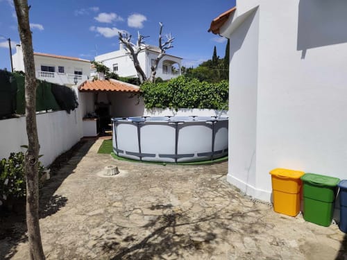Pátio da Albufeira Inn com piscina redonda, edifícios de paredes brancas, árvore sem folhas e caixotes coloridos