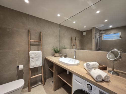 Salle de bain moderne de l'appartement Grimaud Locations Paradise Lagoon avec vanité en bois, lavabo blanc, douche à l'italienne et vue sur mer