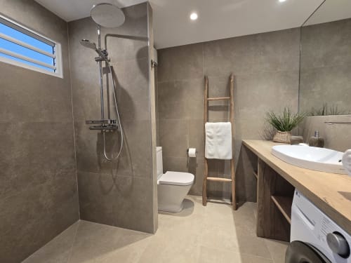 Salle de bains moderne à Grimaud Locations Paradise Lagoon avec douche ouverte, lavabo blanc, toilettes, échelle à serviettes en bois