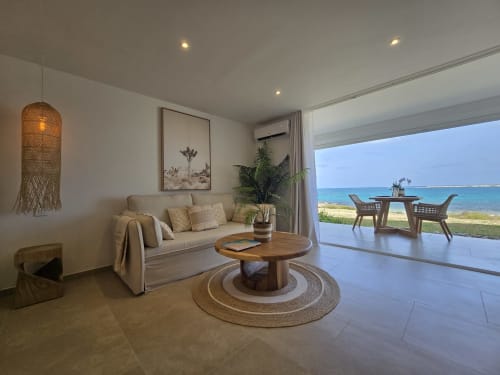 Salon d'appartement en front de mer avec vue sur l'océan, canapé moderne, table en bois et accès direct à la terrasse