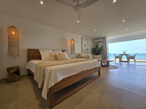 Chambre vue mer Paradise Lagoon avec lit en bois, luminaires suspendus tressés et vue panoramique depuis le balcon chez Grimaud Locations