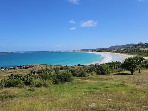 Plage turquoise aux sables blancs de Cul-de-Sac, Saint-Martin, entourée d'une végétation luxuriante et de maisons sur les collines