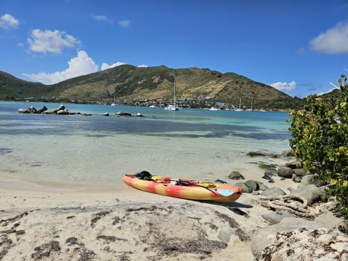 Kayak rouge et jaune sur plage de sable avec lagon turquoise, voiliers et collines verdoyantes à Cul-de-Sac