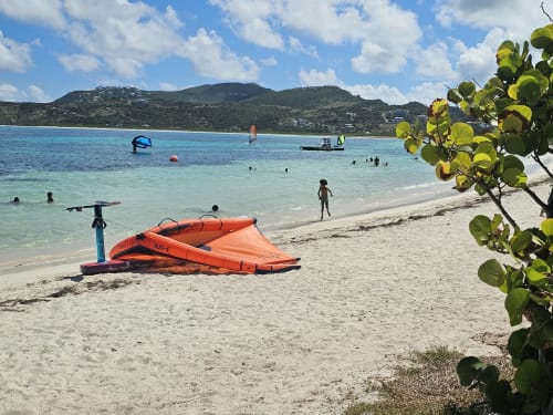 Plage tropicale avec cerf-volant orange, eaux turquoise et collines luxuriantes, lagon paradisiaque de Cul-de-Sac