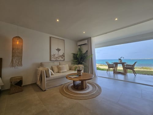 Salon de l'appartement Paradise Lagoon avec vue mer, canapé beige, table en bois et balcon surplombant les eaux turquoise