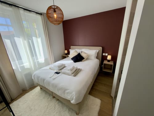 Chambre moderne à la Suite & Appts Le 1 Péraudel à Castres avec lit blanc, mur d'accent bordeaux et lumière naturelle