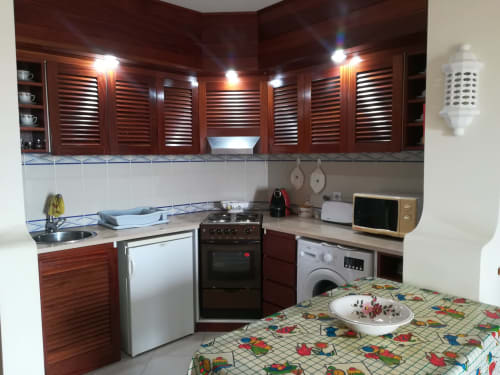 Cozinha compacta em apartamento de Albufeira com armários de madeira vermelha, fogão, máquina de lavar, micro-ondas e mesa de refeições