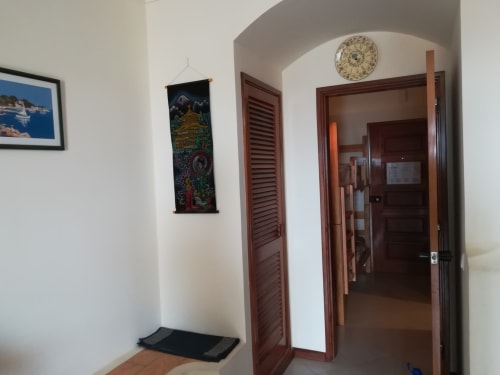 Entrada do apartamento Albufeira Inn com portas de madeira, arco decorativo, tapeçaria e relógio nas paredes brancas