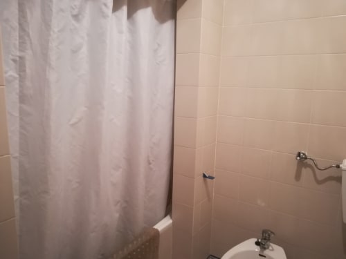 Banheiro da Albufeira Inn com cortina de chuveiro branca, paredes azuleijadas, pia e acabamentos cromados