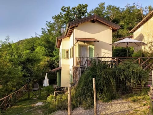 Cream-colored two-level apartment with wooden deck, garden views, and lush greenery at Casa di Cinti B&B in Loiano