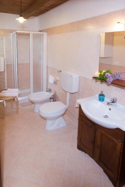 Modern bathroom in Casa di Cinti apartment with white fixtures, pink tile, wooden vanity, shower enclosure, and purple