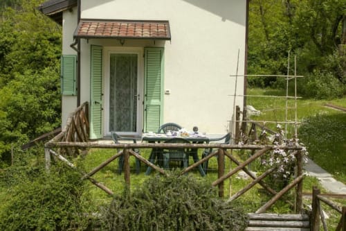 Rustic wooden terrace with dining table at Casa di Cinti apartment in Loiano, surrounded by lush green garden and ivy-covered