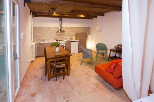 Studio apartment with dining table, orange sofa, kitchen, and wooden beamed ceiling at Casa di Cinti in Loiano