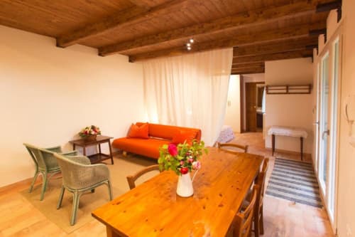 Studio apartment living area at Casa di Cinti with orange sofa, wooden dining table, and exposed beam ceiling in Loiano