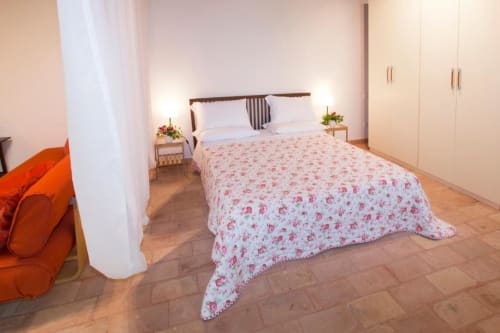 Spacious studio apartment bedroom at Casa di Cinti in Loiano with floral bedding, wooden bed frame, wardrobe, and terracotta
