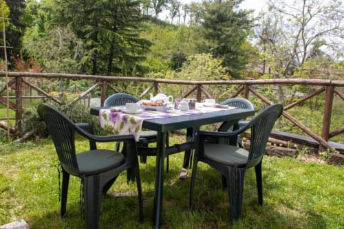 Outdoor dining table with black chairs on garden terrace at Casa di Cinti, Loiano, with forest view
