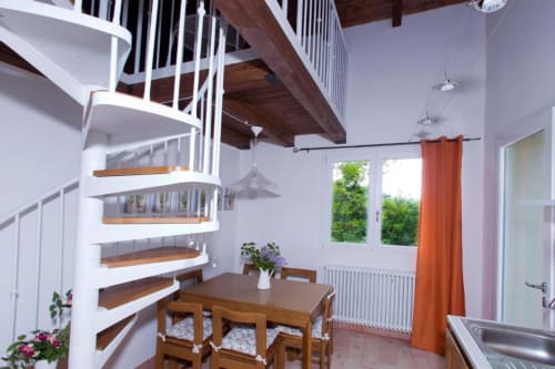 Modern spiral staircase in bright dining area with wooden table, orange curtains, and garden views at Casa di Cinti, Loiano