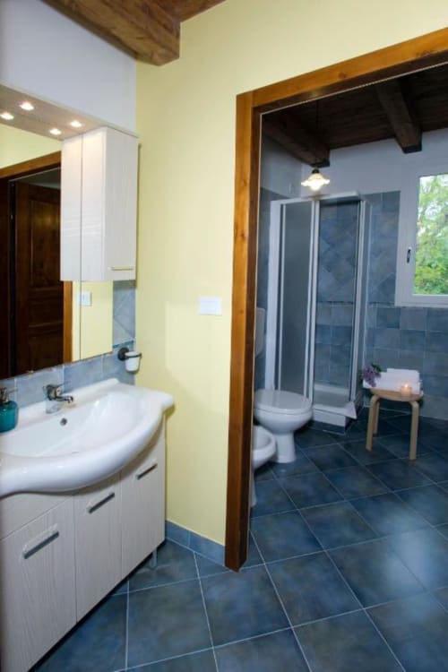 Modern bathroom in Balestruccio apartment at Casa di Cinti, Loiano with yellow walls, white sink and dark tile flooring