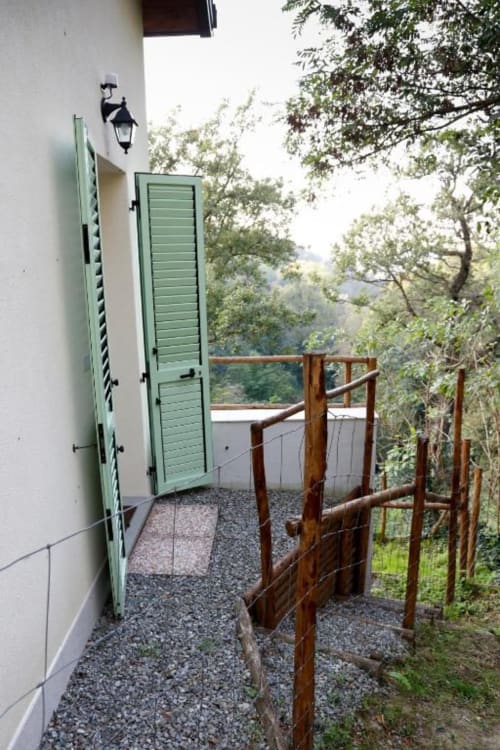Rustic wooden gate entrance to Balestruccio apartment at Casa di Cinti, Loiano, with green shutters and mountain views