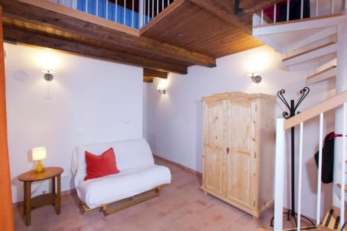 Balestruccio apartment at Casa di Cinti, Loiano: cozy loft with white sofa, wooden beams, natural light, and staircase access