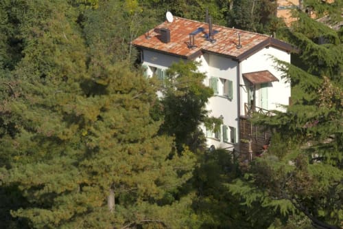 White countryside apartment Casa di Cinti nestled among lush green trees in Loiano, Italy
