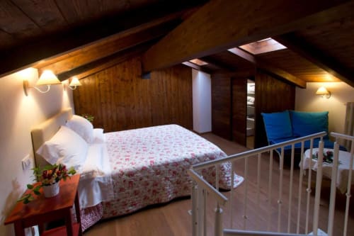 Rustic loft bedroom at Casa di Cinti B&B in Loiano with exposed beams, floral bedding, white pillows, wall sconces, wooden