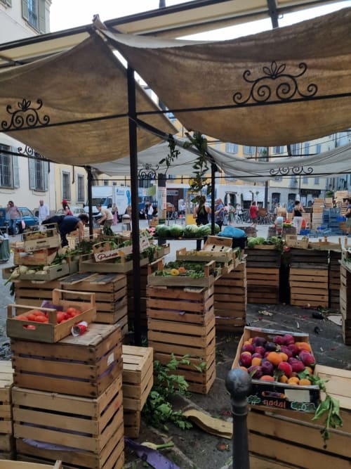 Farmers market stall in Bellano displaying fresh produce in wooden crates under decorative shade awnings