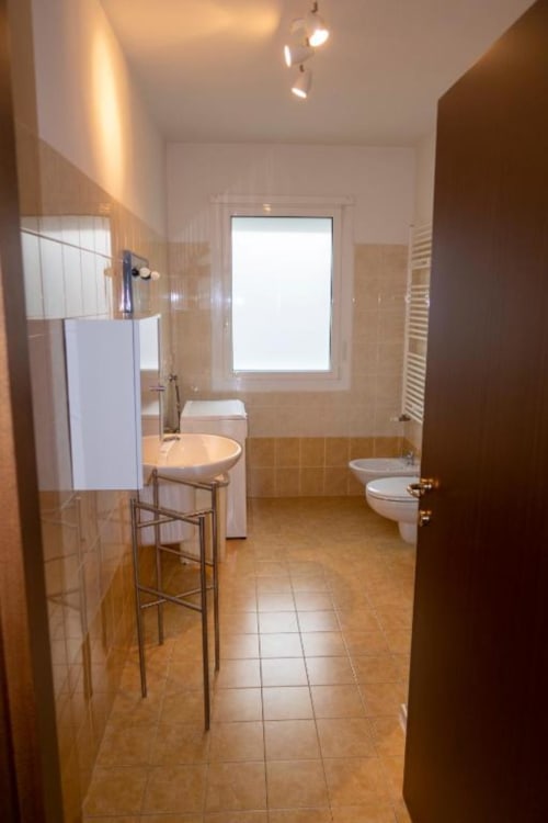 Modern bathroom in Casa di Cinti apartment, Pianoro, with tile flooring, round sink, toilet, bidet, and window to inner