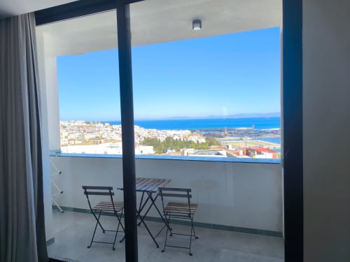 Balcony view from SAMYAflat Tangier apartment overlooking Mediterranean Sea and coastal cityscape with seating area