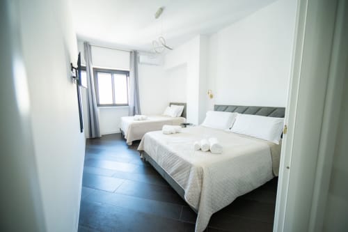 Bright twin bedroom at Newhouse Bari with two double beds, white bedding, gray headboards, and city views.