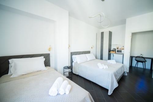 Camera da letto moderna con due letti a Newhouse Bari, biancheria bianca, testiere grigie e comfort contemporanei.