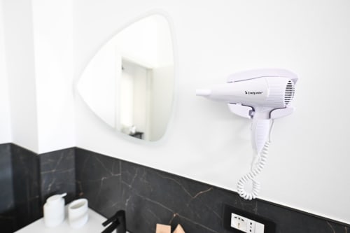 Asciugacapelli bianco montato a parete nel bagno accanto allo specchio della Camera 2 Argiro presso l'hotel Newhouse di Bari