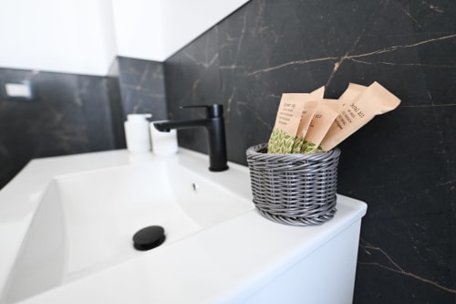 Lavabo moderno con rivestimento in marmo nero, cesto intrecciato con articoli da toilette e rubinetto nero nella camera dell'hotel Newhouse Bari
