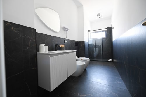 Bagno moderno a Newhouse Bari con pareti in marmo nero, vanità bianca, wc e doccia a filo pavimento