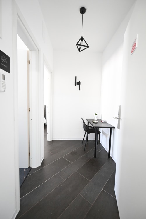 Corridoio minimalista all'hotel Newhouse di Bari con pavimentazione a spina di pesce scura, pareti bianche e luce geometrica a sospensione