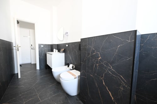 Bagno moderno presso l'hotel Newhouse a Bari con pareti in marmo nero e sanitari bianchi