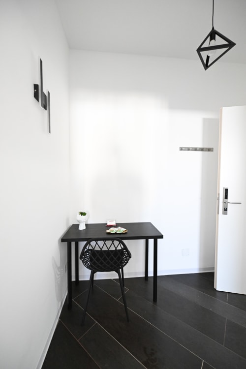 Moderna zona lavoro minimalista nella Room 2 Newhouse Argiro, Bari con scrivania nera, sedia intrecciata e pareti bianche