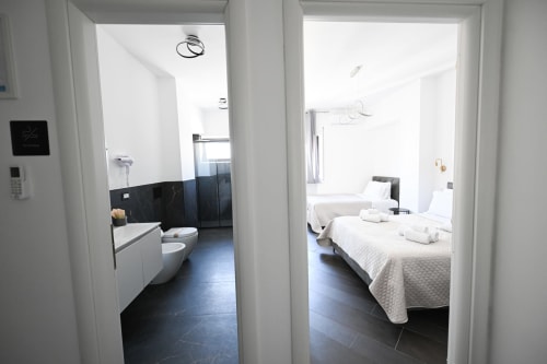 Camera Argiro Room 2 dell'hotel Newhouse a Bari con camera da letto moderna dotata di due letti e bagno adiacente con finiture in piastrelle scure