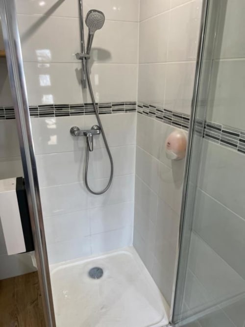 Salle de bain moderne avec carrelage blanc, pommeau de douche effet pluie et mitigeur chromé à la Villa des Palmiers