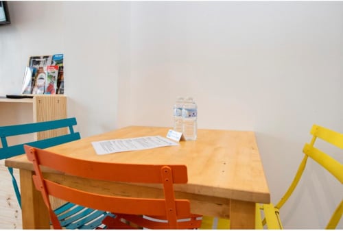 Table de salle à manger en bois avec chaises colorées et bouteille d'eau dans la chambre de la Villa des Palmiers, Villeneuve-sur-Lot